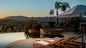 A poolside area with lounge chairs and a view of a sunset over a valley. - Vineyard View by Fieldtrip 8 Bd with Infinity Pool, Hot Tub, Games (Murrieta)