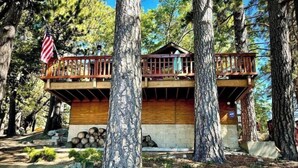 A cabin with a wooden deck, surrounded by tall trees. - Explore. Rest. Restore. (Rimforest)