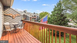 Una terraza de madera con mobiliario exterior, una bandera estadounidense y una escultura de pájaro en la pared.