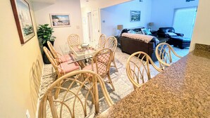 Un comedor con mesa de vidrio y sillas de mimbre, una sala de estar con sofá y mesa de centro, y vistas al exterior.