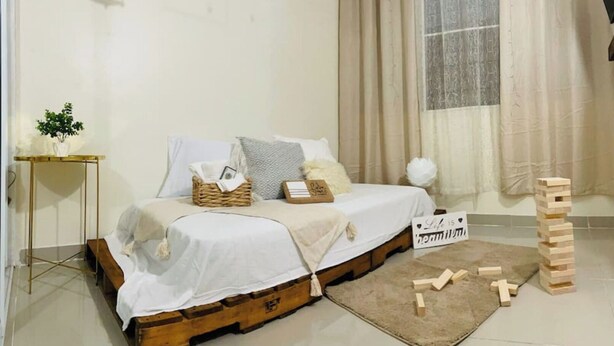 Une chambre avec un lit, une table de chevet et une fenêtre avec des rideaux. Il y a un panneau sur le lit et des blocs de bois sur le sol.