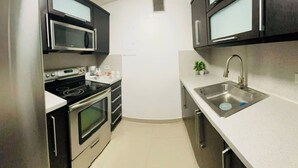 Une cuisine de taille réduite, dotée d’appareils électroménagers en acier inoxydable, d’un évier et de placards.