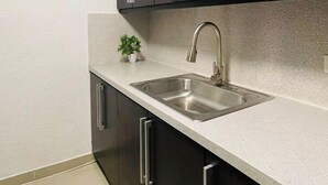Une cuisine moderne avec des meubles de couleur sombre, un évier en acier inoxydable et une petite plante en pot.