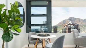 Une chambre moderne avec une table ronde, deux chaises, une plante en pot et une grande fenêtre offrant une vue sur la ville et les montagnes.
