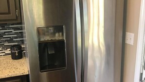 A stainless steel Whirlpool refrigerator with a water and ice dispenser, located in a kitchen with dark cabinets and a granite countertop.