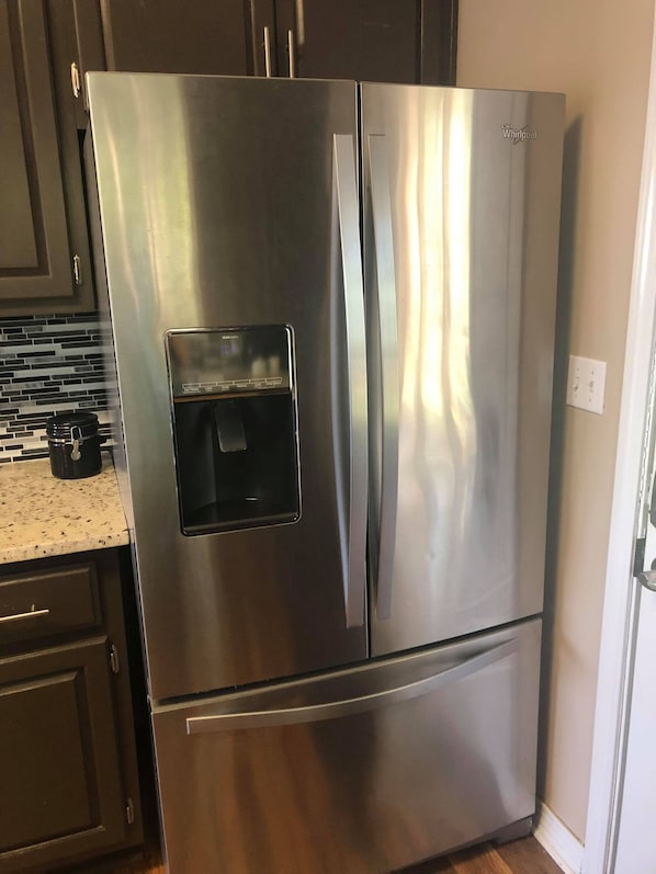 A stainless steel Whirlpool refrigerator with a water and ice dispenser, located in a kitchen with dark cabinets and a granite countertop.