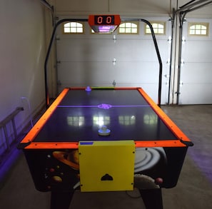 A table tennis table with a digital scoreboard, located in a garage with a door and windows.