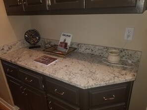A kitchen counter with a granite top, a coffee maker, a tray with a book titled "CULLMAN," and a decorative clock.