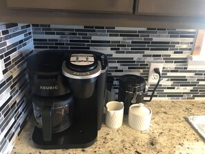 A Keurig coffee maker, a black coffee pot, two white mugs, and a black coffee pot on a kitchen counter with a tiled backsplash.