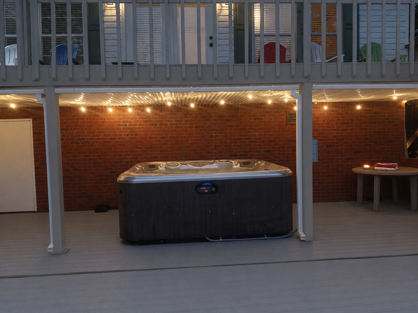 A hot tub under a covered area with a brick wall and string lights.