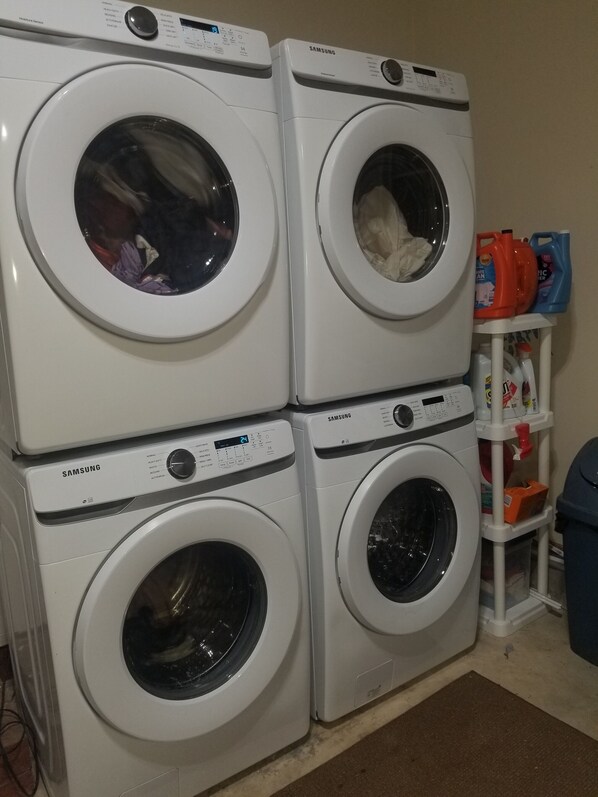 A stack of four white Samsung washing machines in a laundry room.