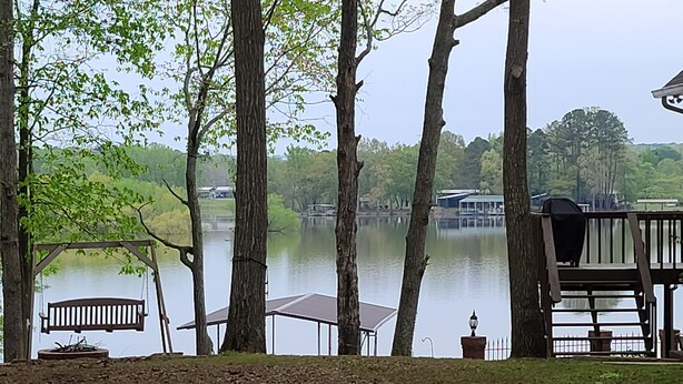 A lakeside view with a wooden deck, a swing, and a covered picnic table.