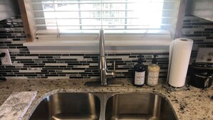 A kitchen with a double stainless steel sink, a window with blinds, and two bottles of dish soap.