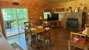 L’intérieur d’un chalet en bois comprend un coin repas, un téléviseur, une cheminée et un mur en pierre.