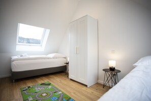 Un dormitorio con cama, armario, una mesita de noche con lámpara, ventana y alfombra.