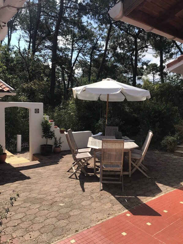 Relax in a serene outdoor space surrounded by lush greenery and trees, with a shaded patio area featuring a table and chairs.
