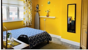 A bedroom with a bed, a desk, a chair, a mirror, and a window with curtains.