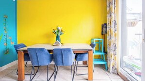 A dining area with a yellow wall, a wooden table, and blue chairs.