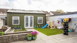 A backyard with a green shed, a small play area with a slide, and a garden with potted plants.