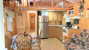 A cozy cabin-style kitchen with wooden cabinets, a dining table with chairs, a kitchenette, and a loft bedroom area. - Assoc beach, Lakes, Naples Causeway, restaurants, shops, boat- jet ski rentals. (Naples)