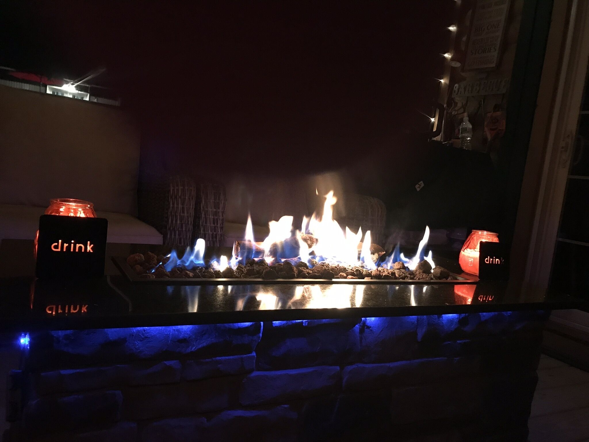 Een bar met een stenen muur, een open haard en twee verlichte borden met 'drink' erop.