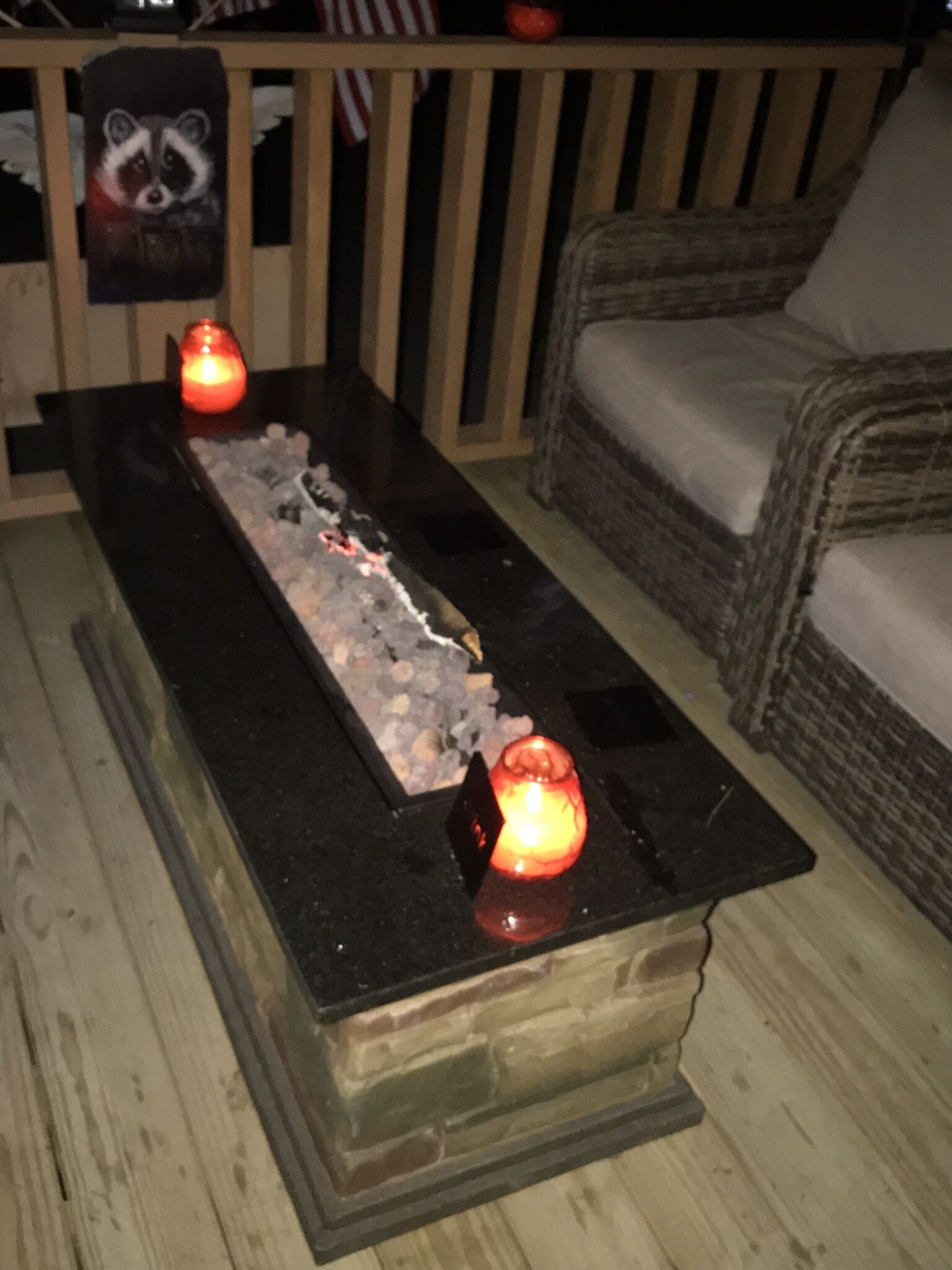 A wooden deck with a fire feature in the center, surrounded by wicker furniture.
