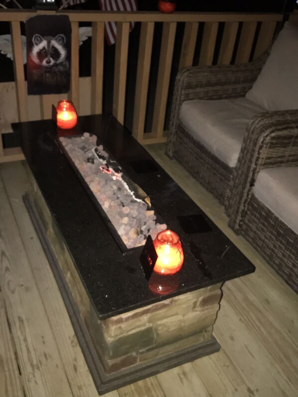 Una terraza de madera con una chimenea en el centro, rodeada de mobiliario de mimbre.