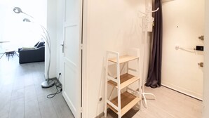 Ein Zimmer mit einer weißen Tür, einem weißen Regalschrank, einem dunklen Vorhang und einem kleinen Tisch mit einer Lampe.
