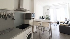 Eine moderne Küche mit Einbauofen, Mikrowelle und Herd. Eine Waschmaschine sowie ein Essbereich mit Tisch und Stühlen sind vorhanden.