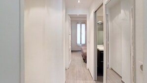 Ein schmaler, gut beleuchteter Flur mit Holzboden, der zu einem Zimmer mit Bett und Bad führt.