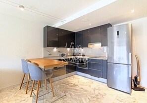 Cozinha moderna com mesa e cadeiras de madeira, geladeira de aço inoxidável e armários escuros.