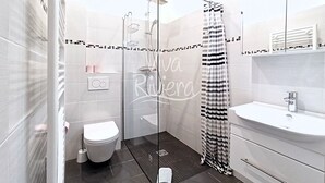 Ein modernes Badezimmer mit einer gläsernen Duschkabine, einer weißen Toilette und einem Waschbecken mit Spiegel darüber.