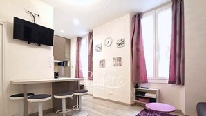 Ein modernes Wohnzimmer mit einem Wand-Fernseher, einer Bar mit Sitzhocker, einem violetten Teppich und einem Fenster mit Vorhängen.