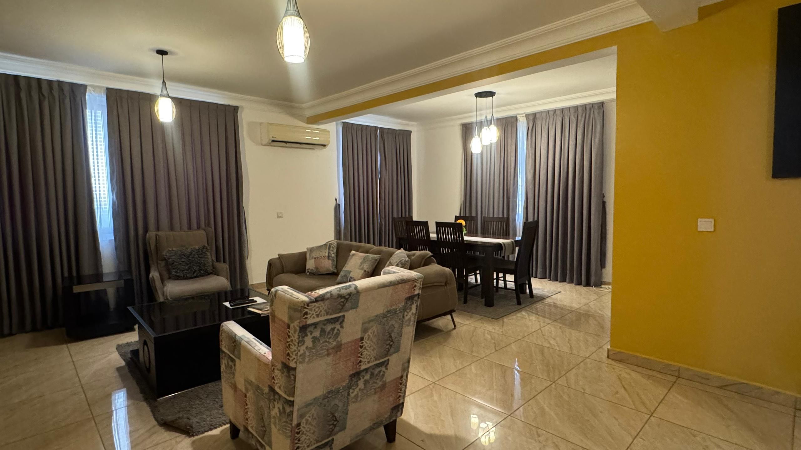 A living room with a sofa, a coffee table, and a dining area with a table and chairs.