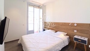 A bedroom with a large bed, a nightstand, a TV mounted on the wall, and a sliding glass door leading to an outdoor area. - Viva Riviera Rue Hoche Luxury Collection (Cannes)