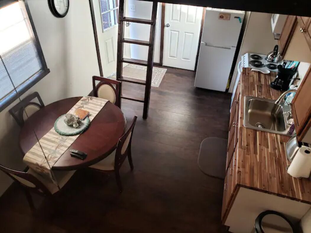 Une cuisine compacte avec un plancher en bois, un coin repas avec une table et des chaises, et un réfrigérateur à l’arrière-plan.