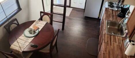 Une cuisine compacte avec un plancher en bois, un coin repas avec une table et des chaises, et un réfrigérateur à l’arrière-plan.