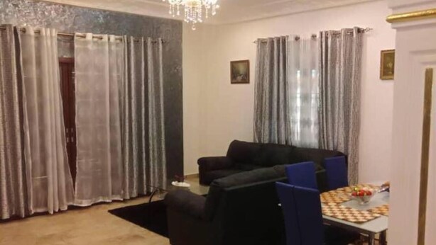 A living room with a black sofa, a dining table with blue chairs, and a chandelier.