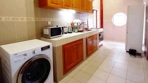 A compact kitchen with wooden cabinets, a washing machine, and a microwave.