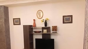 A living room with a flat-screen TV on a wooden stand, a vase with flowers, and two framed pictures on the wall.