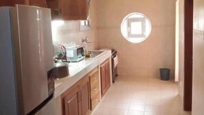 A kitchen with wooden cabinets, a stainless steel refrigerator, a sink, and a window with a view.