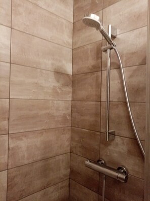 Un coin d’une salle de bain avec une zone de douche, comprenant une douchette à main et un robinet fixé au mur.