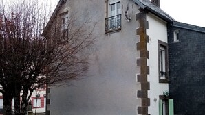 A building with a grey exterior and a black roof, featuring a small balcony and a door with shutters. - Beautiful ground-floor apartment rated 3 keys by Clévacances. Private, enclosed garden. (Mont-Dore)