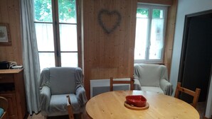 A cozy dining area with a wooden table and chairs, a heart-shaped decoration on the wall, and a window with curtains. - Beautiful ground-floor apartment rated 3 keys by Clévacances. Private, enclosed garden. (Mont-Dore)