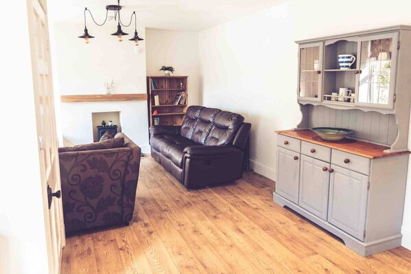 A living room with a leather sofa, patterned armchair, wooden flooring, and a built-in cabinet with shelves. - 3-bed Cottage-plymouth-dog Friendly-sleeps7 (Plymouth)