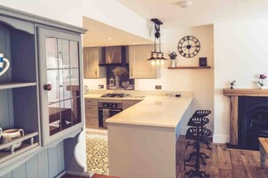 A modern kitchen with a central island, a dining area with bar stools, and a decorative clock on the wall.