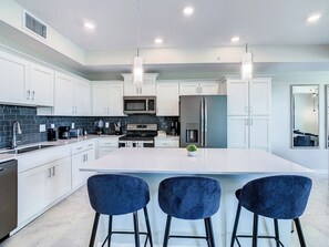 A modern kitchen with white cabinetry, stainless steel appliances, and a central island with bar stools.