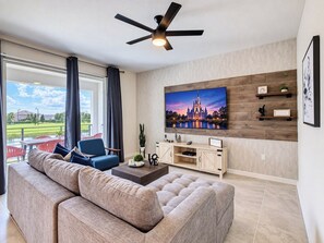 A modern living room with a large sofa, a coffee table, and a flat-screen TV mounted on a wooden wall.