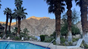 A pool area with lounge chairs, palm trees, and a mountainous backdrop. - Condo with amazing views and 3 pools (Indian Wells)
