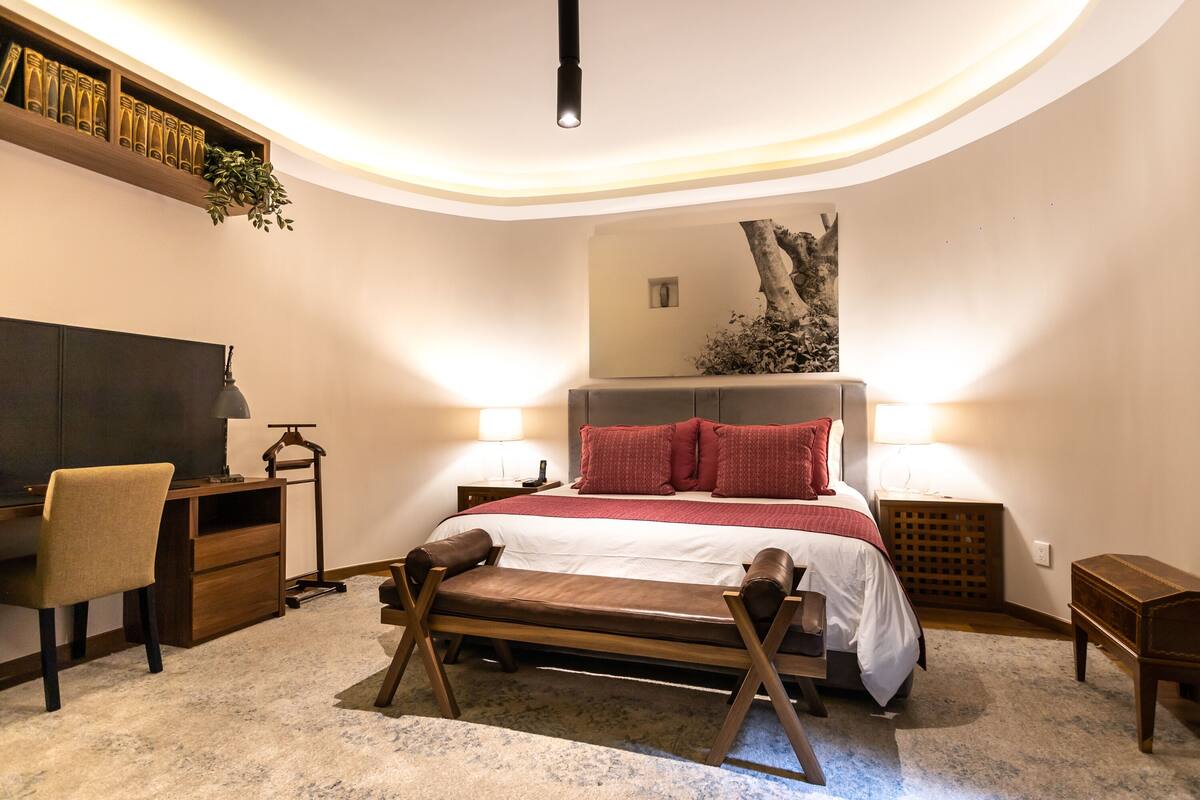 Um quarto moderno com teto curvo, uma cama com roupa de cama vermelha, uma escrivaninha com cadeira e uma estante de livros.